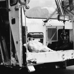 close up view of the front and a bit of the side of a nyc garbage truck. the truck is partially covered in snow and looks particularly brutalist in the black and white rendering