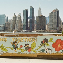 a picture of a cartoon mural of a diverse cast of kids playing on a big flower tilted sideways with an older lady with a walker smelling the flower contentedly. a cat basks under a leaf as a dog uses a watering can to nurture a seedling. behind the mural, in the background, is the new york skyline as seen from long island city.