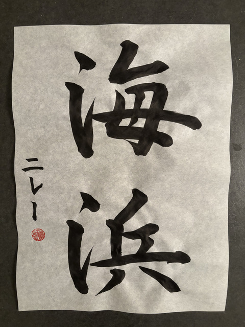 vertically written japanese calligraphy in black ink on white paper, with a signature and red seal on the left side